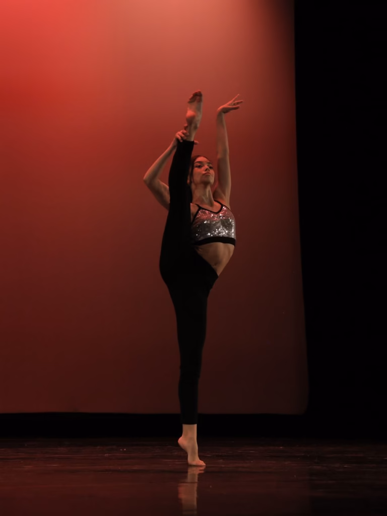 Bailarina de la academia en penché sobre el escenario, ante el telón rojo